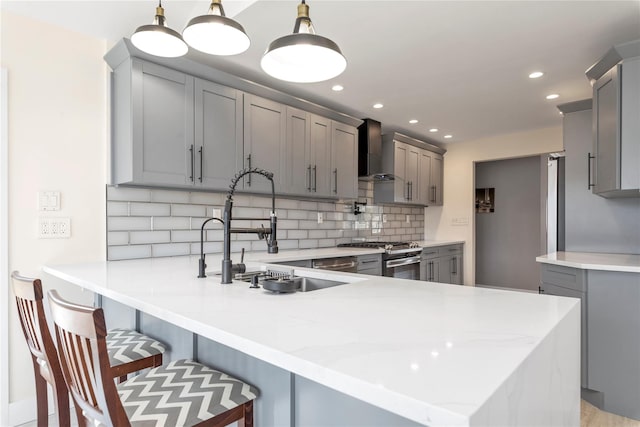 kitchen with gray cabinetry, a peninsula, gas stove, wall chimney exhaust hood, and a sink