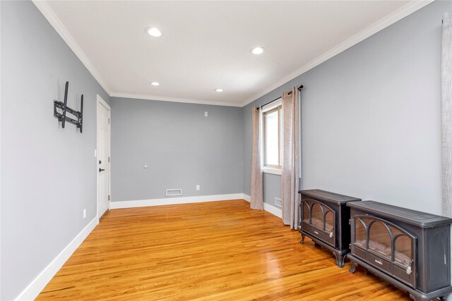 empty room with visible vents, baseboards, ornamental molding, a wood stove, and light wood-style floors