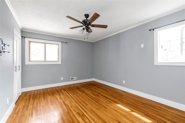 empty room with visible vents, light wood-style floors, crown molding, baseboards, and ceiling fan