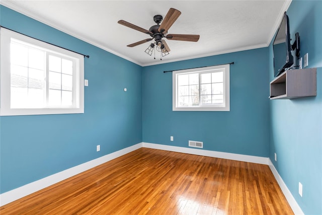 empty room featuring visible vents, baseboards, ornamental molding, and hardwood / wood-style flooring