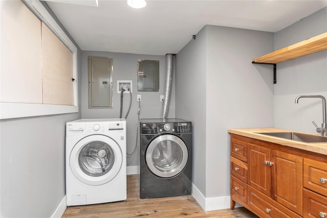 clothes washing area with a sink, separate washer and dryer, electric panel, and light wood-style flooring