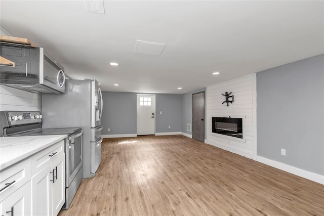 kitchen featuring baseboards, light wood-style flooring, stainless steel range with electric cooktop, a fireplace, and white cabinetry