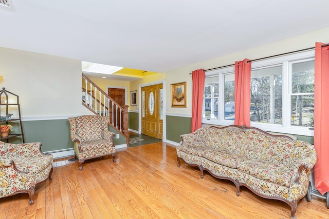 sitting room with a baseboard radiator, wood-type flooring, baseboards, and stairs