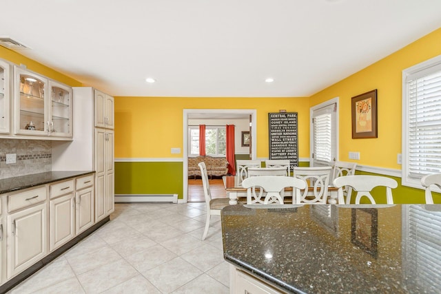 kitchen featuring visible vents, a baseboard heating unit, tasteful backsplash, light tile patterned floors, and glass insert cabinets