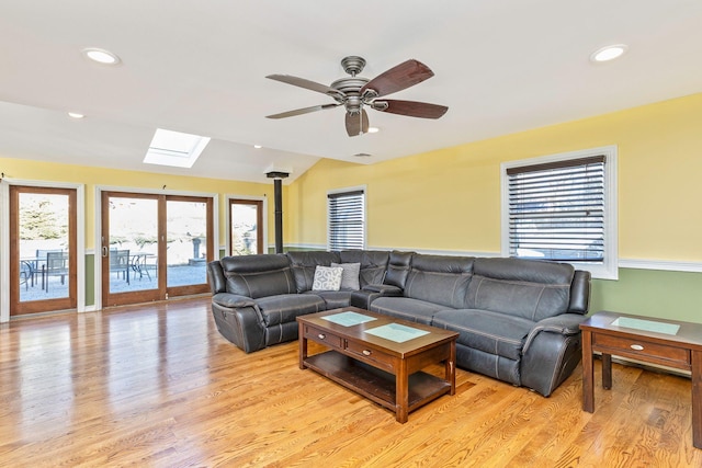 living room with vaulted ceiling with skylight, recessed lighting, light wood-type flooring, and a wealth of natural light