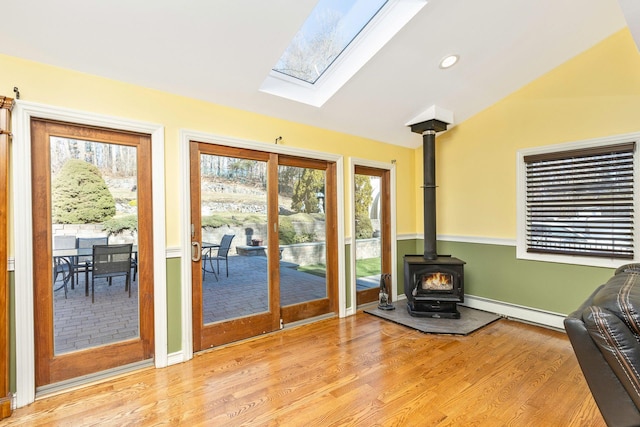 entryway with light wood-type flooring, lofted ceiling with skylight, recessed lighting, a baseboard radiator, and a wood stove