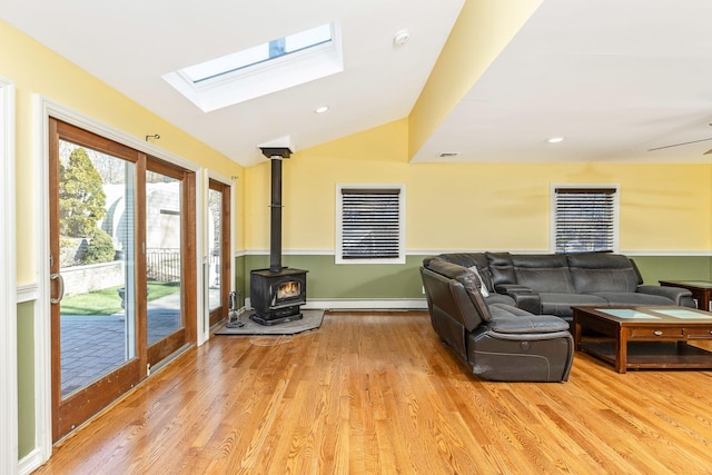 living area featuring a baseboard heating unit, lofted ceiling with skylight, light wood-style flooring, and a wood stove