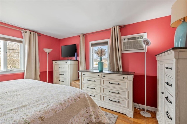 bedroom featuring light wood finished floors, baseboards, and a wall unit AC