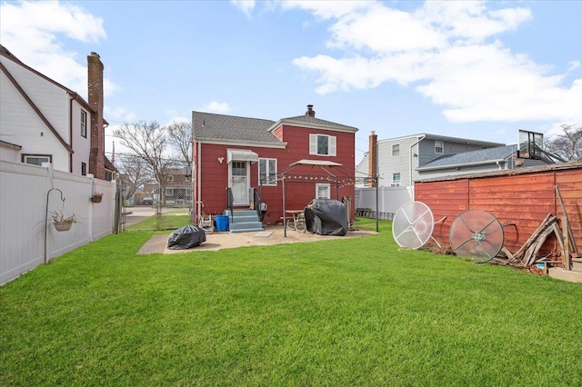 rear view of property with a lawn, entry steps, a chimney, and a fenced backyard