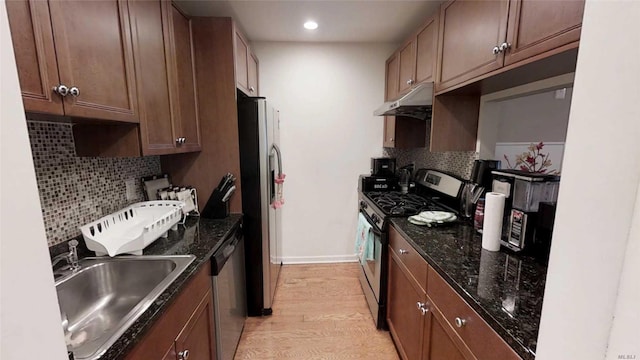 kitchen with light wood finished floors, a sink, decorative backsplash, under cabinet range hood, and appliances with stainless steel finishes