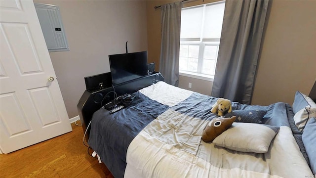 bedroom with electric panel, baseboards, and wood finished floors