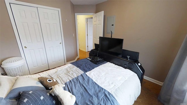 bedroom featuring wood finished floors, electric panel, baseboards, and a closet