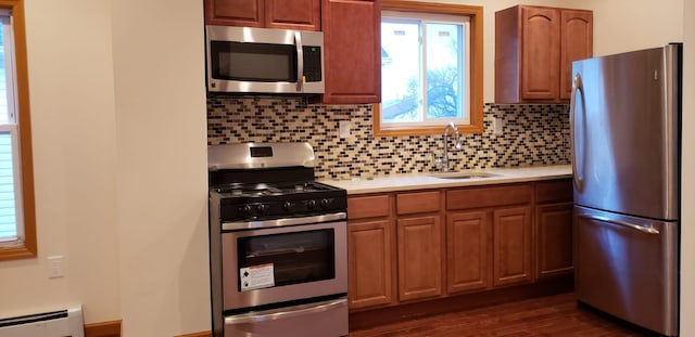 kitchen with a sink, light countertops, decorative backsplash, stainless steel appliances, and a baseboard radiator