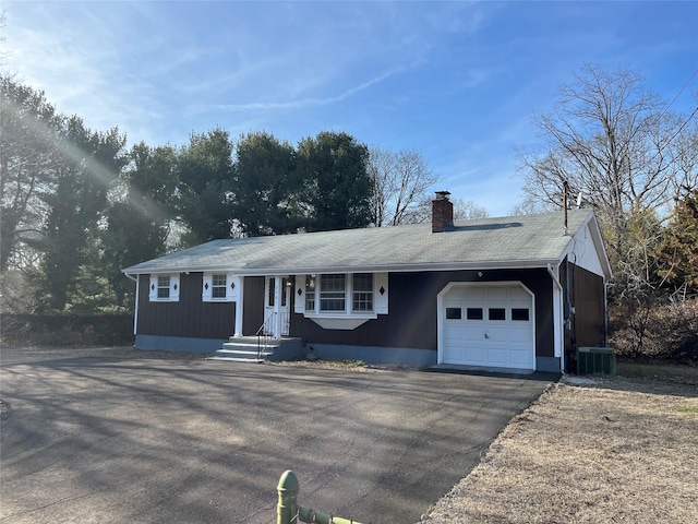 ranch-style home featuring aphalt driveway, an attached garage, central AC unit, and a chimney