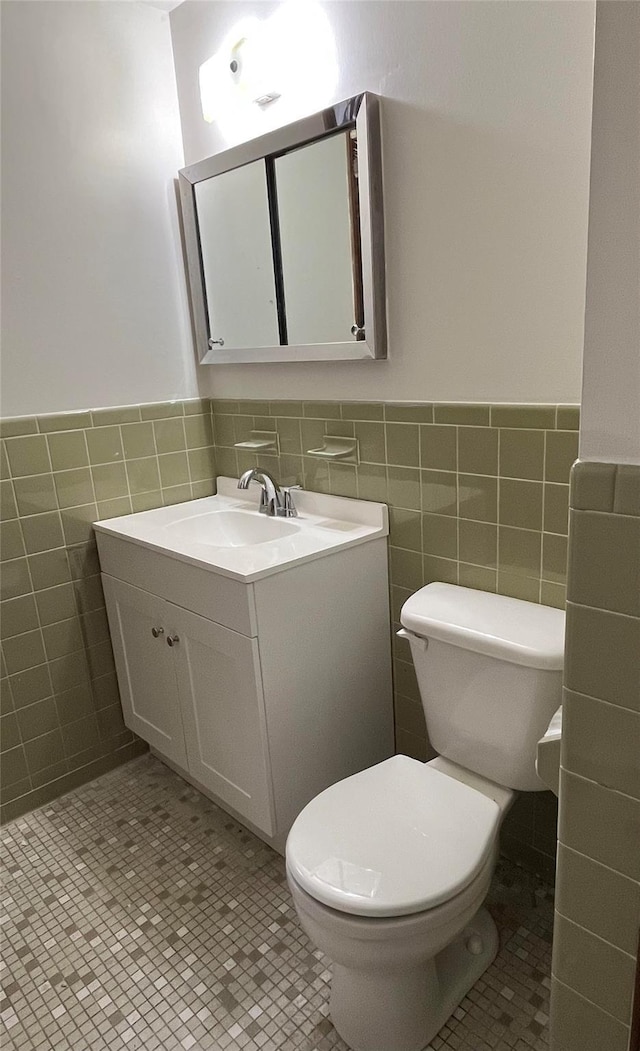 half bathroom with vanity, wainscoting, tile walls, toilet, and tile patterned floors