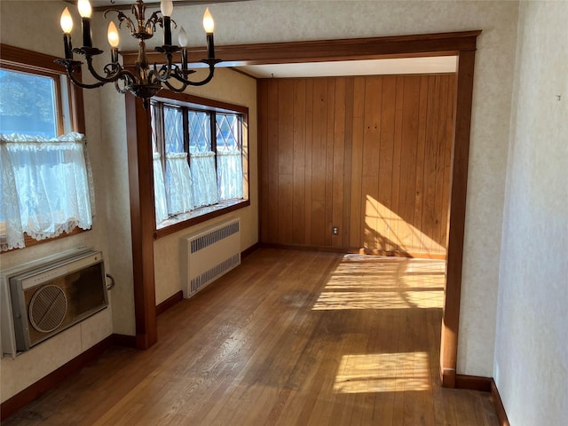 unfurnished dining area featuring baseboards, wood-type flooring, radiator, and a chandelier