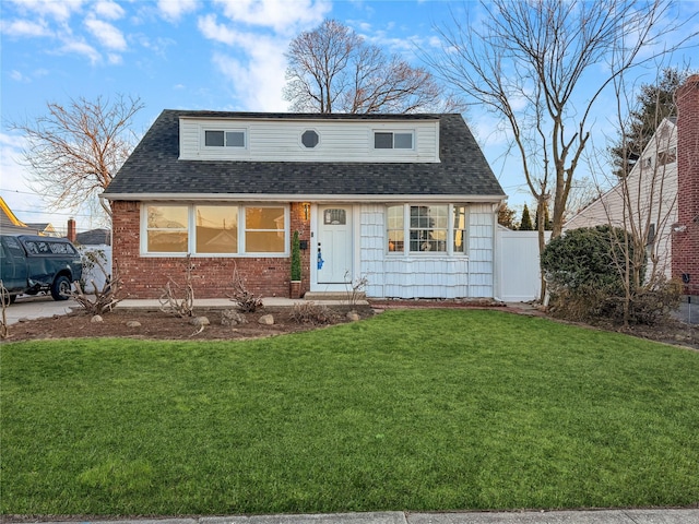 view of front of home with brick siding, a shingled roof, a front yard, and fence