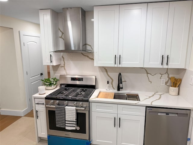 kitchen with decorative backsplash, white cabinets, stainless steel appliances, wall chimney exhaust hood, and a sink