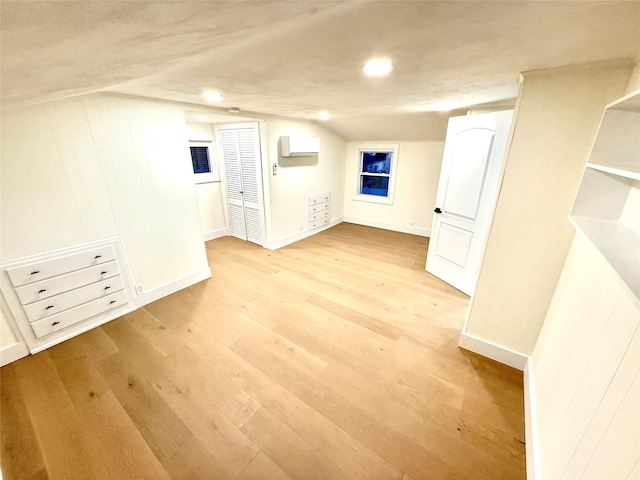 empty room with light wood-type flooring, baseboards, vaulted ceiling, and a wall unit AC