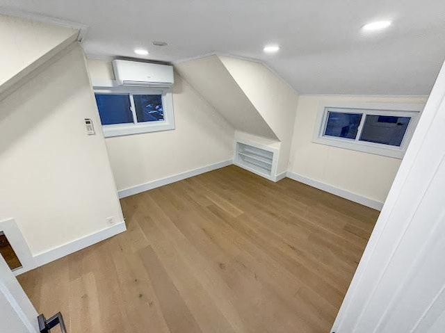 additional living space featuring baseboards, a wall mounted air conditioner, lofted ceiling, and wood finished floors