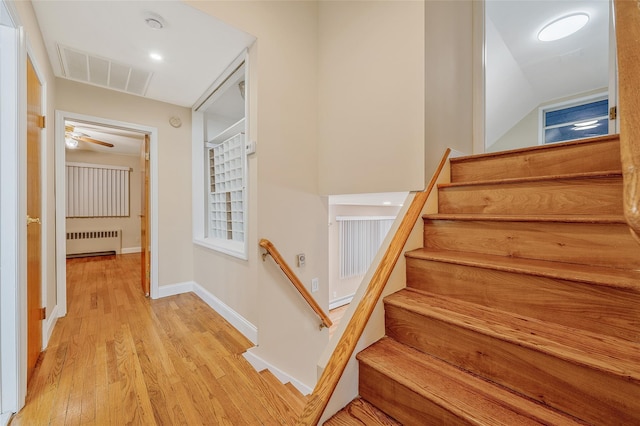 stairway with visible vents, baseboards, wood finished floors, and radiator heating unit