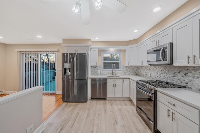 kitchen with light wood finished floors, appliances with stainless steel finishes, light countertops, and a sink