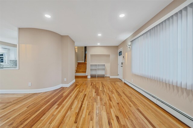 unfurnished living room featuring light wood-style floors, baseboards, baseboard heating, and stairs