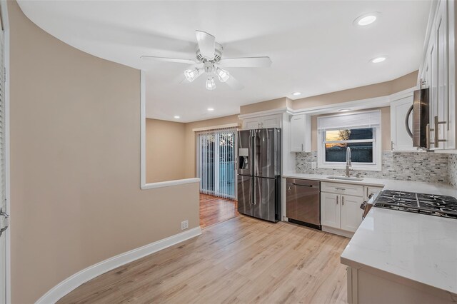 kitchen with light wood finished floors, backsplash, baseboards, stainless steel appliances, and a sink