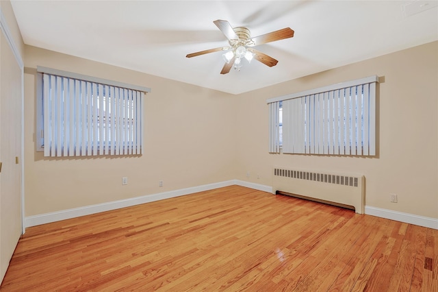 empty room with a wealth of natural light, light wood-type flooring, baseboards, and radiator heating unit