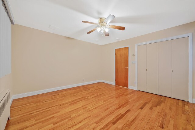 unfurnished bedroom featuring light wood-style floors, baseboards, radiator, and a closet