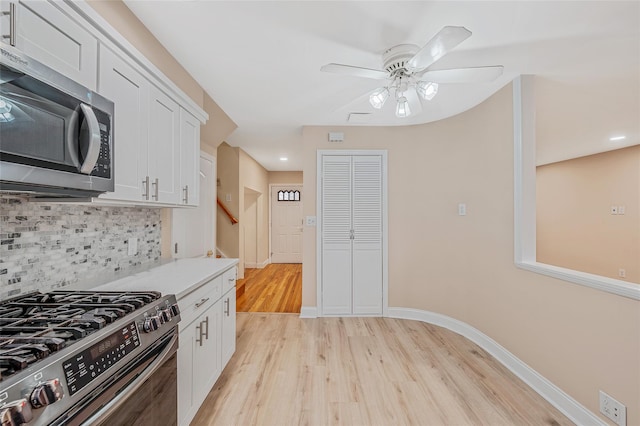 kitchen featuring baseboards, light wood finished floors, white cabinets, appliances with stainless steel finishes, and backsplash