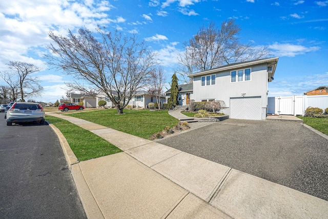 view of front of property featuring a front lawn, fence, aphalt driveway, a residential view, and a gate