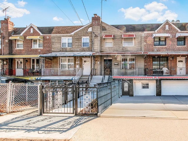 multi unit property featuring a fenced front yard, stone siding, driveway, and an attached garage