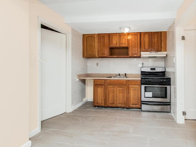 kitchen featuring under cabinet range hood, brown cabinets, gas stove, and a sink