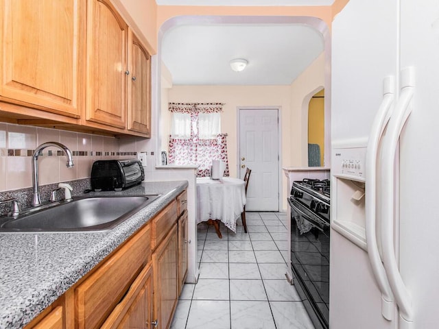 kitchen featuring black gas range oven, backsplash, light stone countertops, white fridge with ice dispenser, and a sink