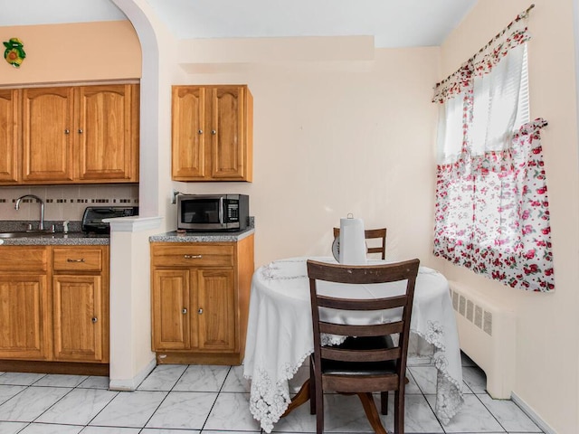 kitchen featuring stainless steel microwave, radiator, brown cabinetry, and tasteful backsplash