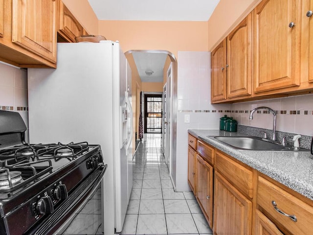 kitchen featuring decorative backsplash, arched walkways, black range with gas cooktop, marble finish floor, and a sink