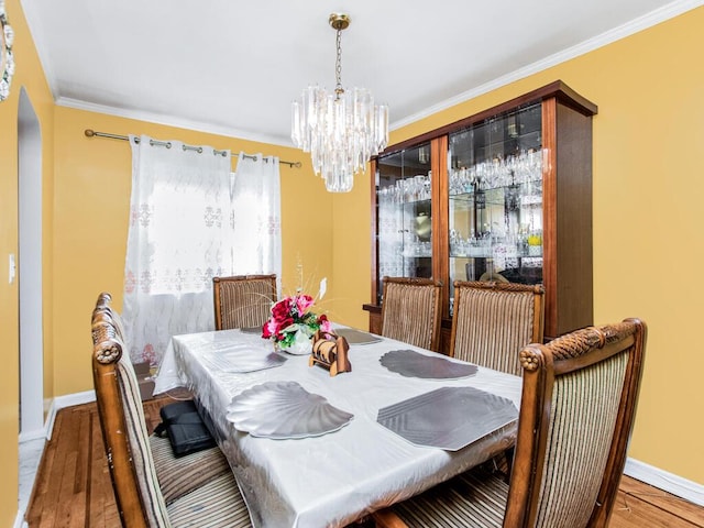 dining space with baseboards, ornamental molding, wood finished floors, arched walkways, and a notable chandelier