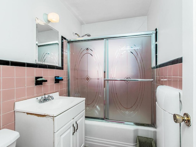 full bath featuring shower / bath combination with glass door, tile walls, vanity, and toilet