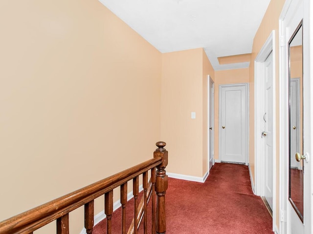 hall with an upstairs landing, baseboards, and dark colored carpet