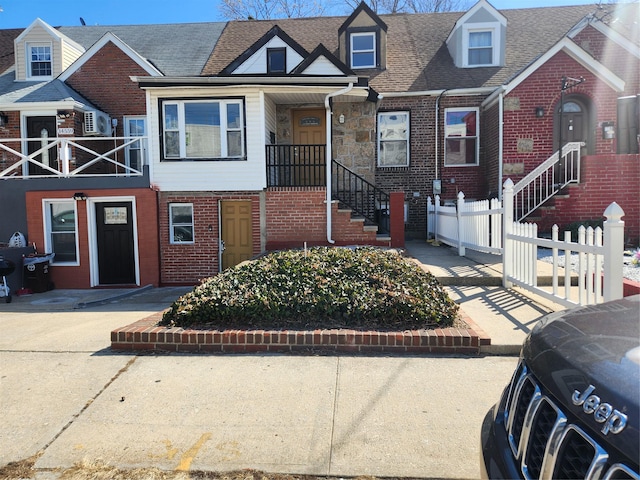 view of property featuring brick siding, roof with shingles, and fence