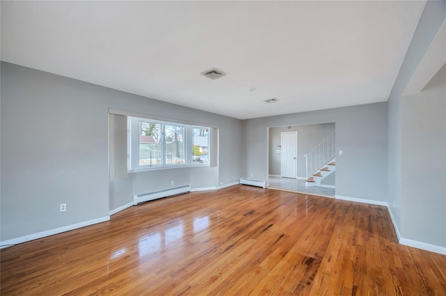 empty room with stairway, wood finished floors, visible vents, and a baseboard radiator