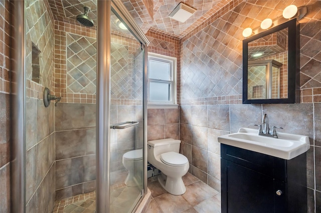 bathroom with tile patterned floors, toilet, tile walls, a shower stall, and vanity