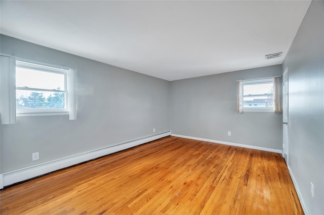 empty room with visible vents, light wood-style flooring, a baseboard heating unit, and baseboards