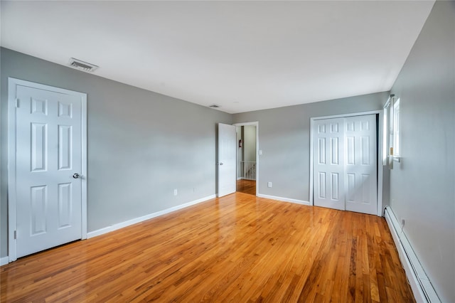 unfurnished bedroom featuring wood finished floors, visible vents, baseboards, a closet, and a baseboard heating unit