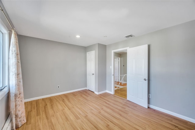 empty room featuring baseboards, visible vents, light wood finished floors, and a baseboard radiator