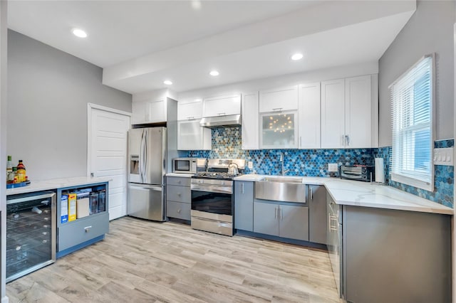 kitchen featuring beverage cooler, under cabinet range hood, light stone counters, a sink, and appliances with stainless steel finishes