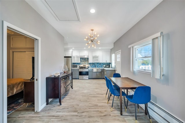 kitchen featuring decorative backsplash, light wood-style floors, appliances with stainless steel finishes, white cabinetry, and baseboard heating