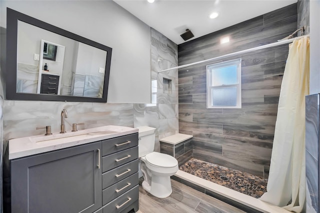 bathroom with toilet, tile walls, vanity, and a tile shower