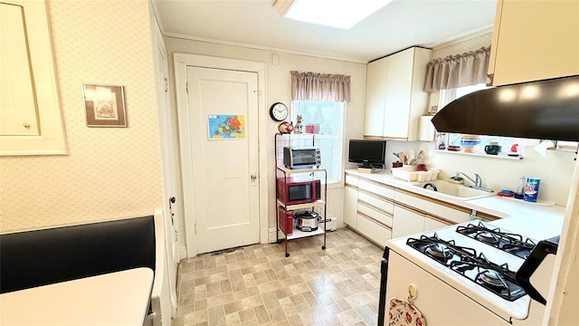 kitchen featuring wallpapered walls, light countertops, white gas range, and a sink